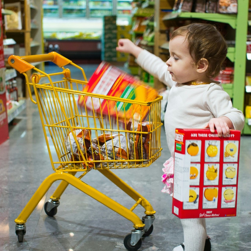 Toddler in a small grocery cart holding a snack box